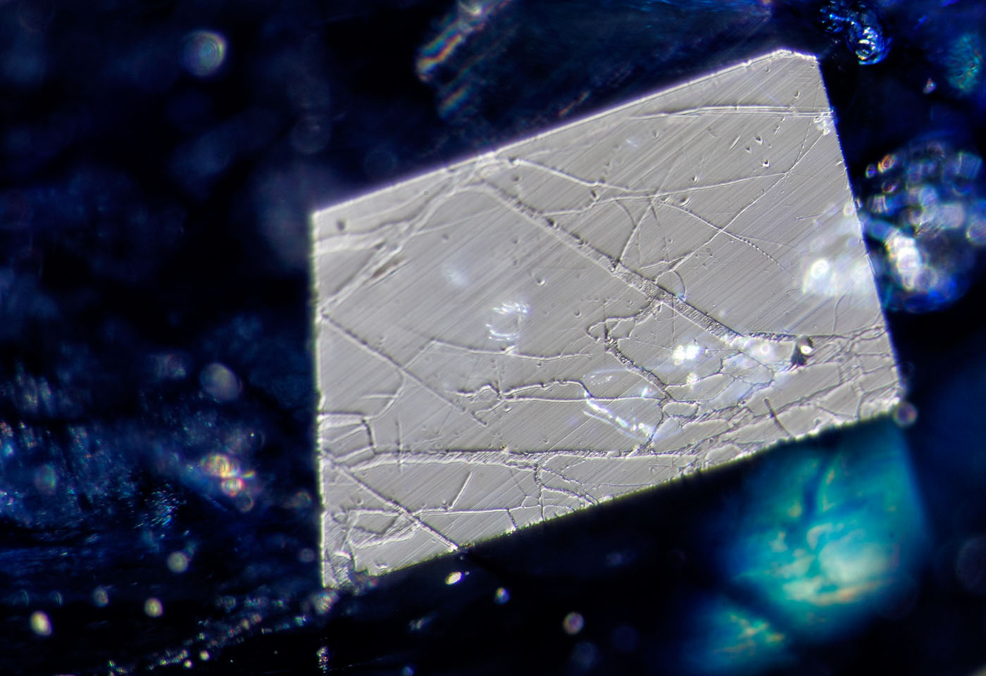 Figure 10. A small facet viewed in reflected light reveals a network of fissures filled with glass. The low hardness of the glass shows serious undercutting compared with the surrounding sapphire. Surface-incident fiber-optic illumination. Photo: Wimon Manorotkul