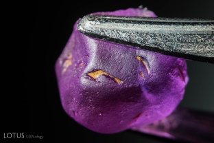 At first glance this Verneuil flame fusion synthetic pink sapphire makes for a convincing piece of natural sapphire rough. The stone has been treated to have a rough surface, complete with naturals with residues inside them meant to look like dirt or matrix. Substances such as shoe polish may be used on the outside of  synthetic “rough” to make it look like natural material.