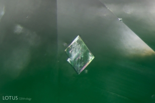 This crystal, suspended in a Colombian emerald, has sharp angular features. Micro Raman identified it as calcite. Note that twin planes are visible in crossed polars.