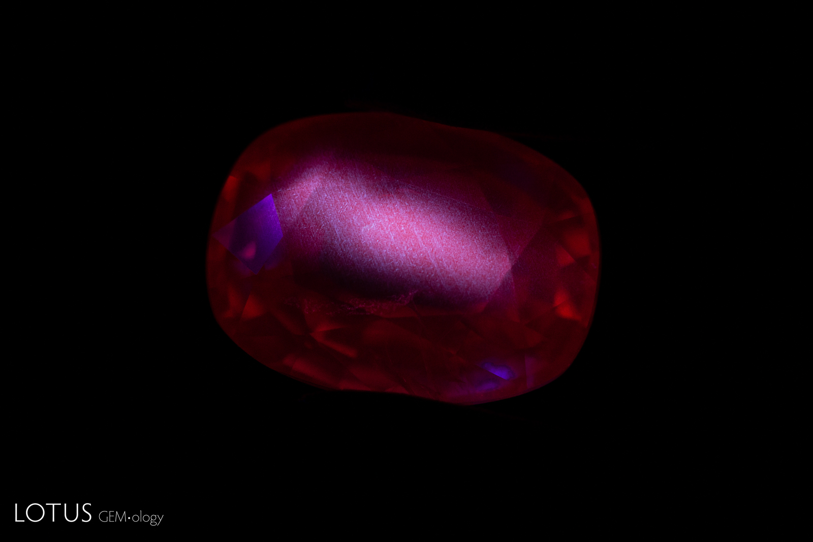 Figure 5. A heated Myanmar ruby displays red fluorescence with clear zoned chalky areas correlated with partially dissolved silk in the stone. Photo: E. Billie Hughes/Lotus Gemology.