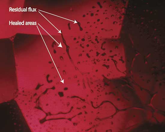 Figure 6. Flux-healed fracture Moderate magnification reveals a flux-healed fracture in a Mong Hsu ruby from Burma. The irregular dark areas are pockets of residual flux, while the red areas in between are where the once open fracture has healed shut with microscopic amounts of what is essentially synthetic ruby. In some places, the flux residue appears transparent. This is an illusion produced by reflection off the surfaces of the flux pockets. Photo: R.W. Hughes