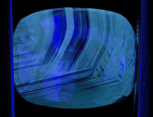 Figure 4. Another blue sapphire showing chalky fluorescence corresponding to the colorless portions of the gem. When seen, this strong chalky blue to green SW fluorescence is an extremely strong indication that the gem has been subjected to high-temperature heat treatment. Note that this fluorescence often appears in patterns that resemble the graining of wood. Photo: Richard W. Hughes; Nikon D200