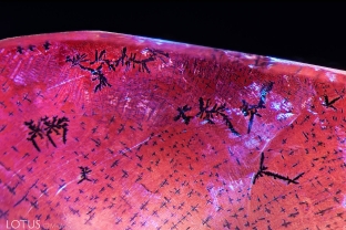 This synthetic pink sapphire was fractured and then appeared to have been soaked in an iron-rich solution to created orange stains in the fissures, thus simulating padparadscha. The stains developed unusual dendritic patterns, as seen here. This fissure also shows an unusual glossy appearance. Chemical analysis also reveal traces of lead in the fissures.