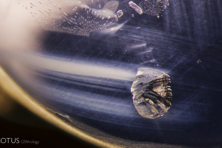 A metallic crystal zooms across an azure sky with small negative crystals and undissolved rutile silk needles providing a dramatic backdrop.