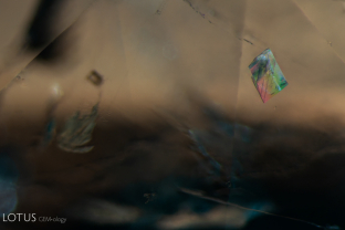 When viewed in crossed polars, this calcite crystal (identified with micro Raman) displays interference colors and polysynthetic twin planes. This calcite is ensconced in an emerald from Colombia.